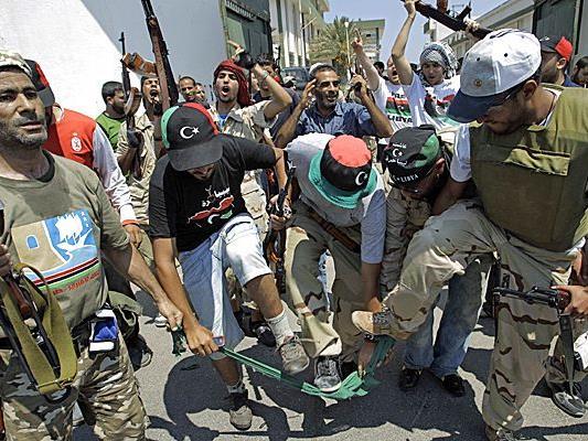 Rebellenkämpfer zerreißen eine grüne Flagge, das Symbol für die Ära Gaddafi.