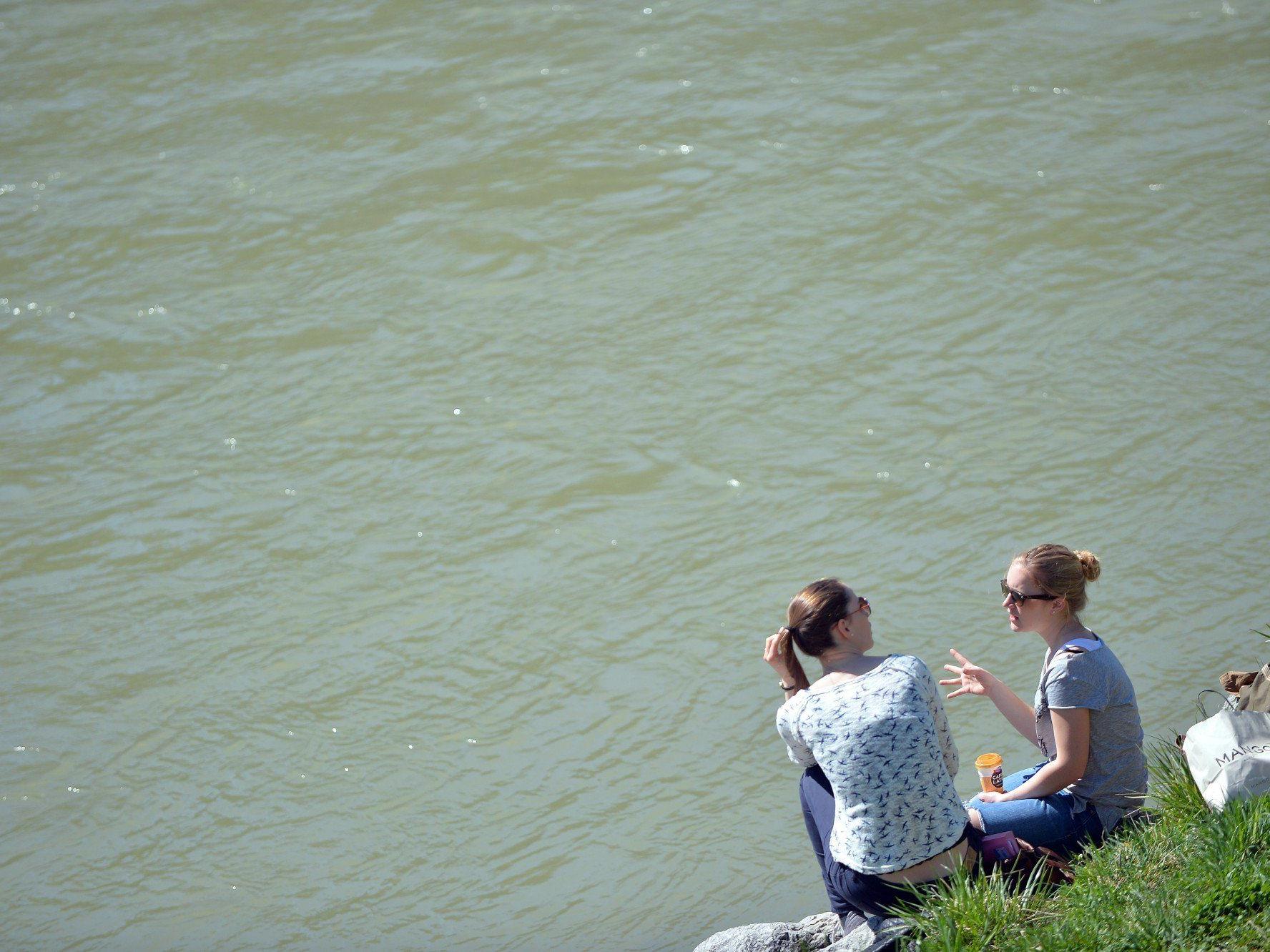 Bei frühsommerlichen Temperaturen sitzen am Montag zwei Mädchen in Salzburg am Salzachufer.