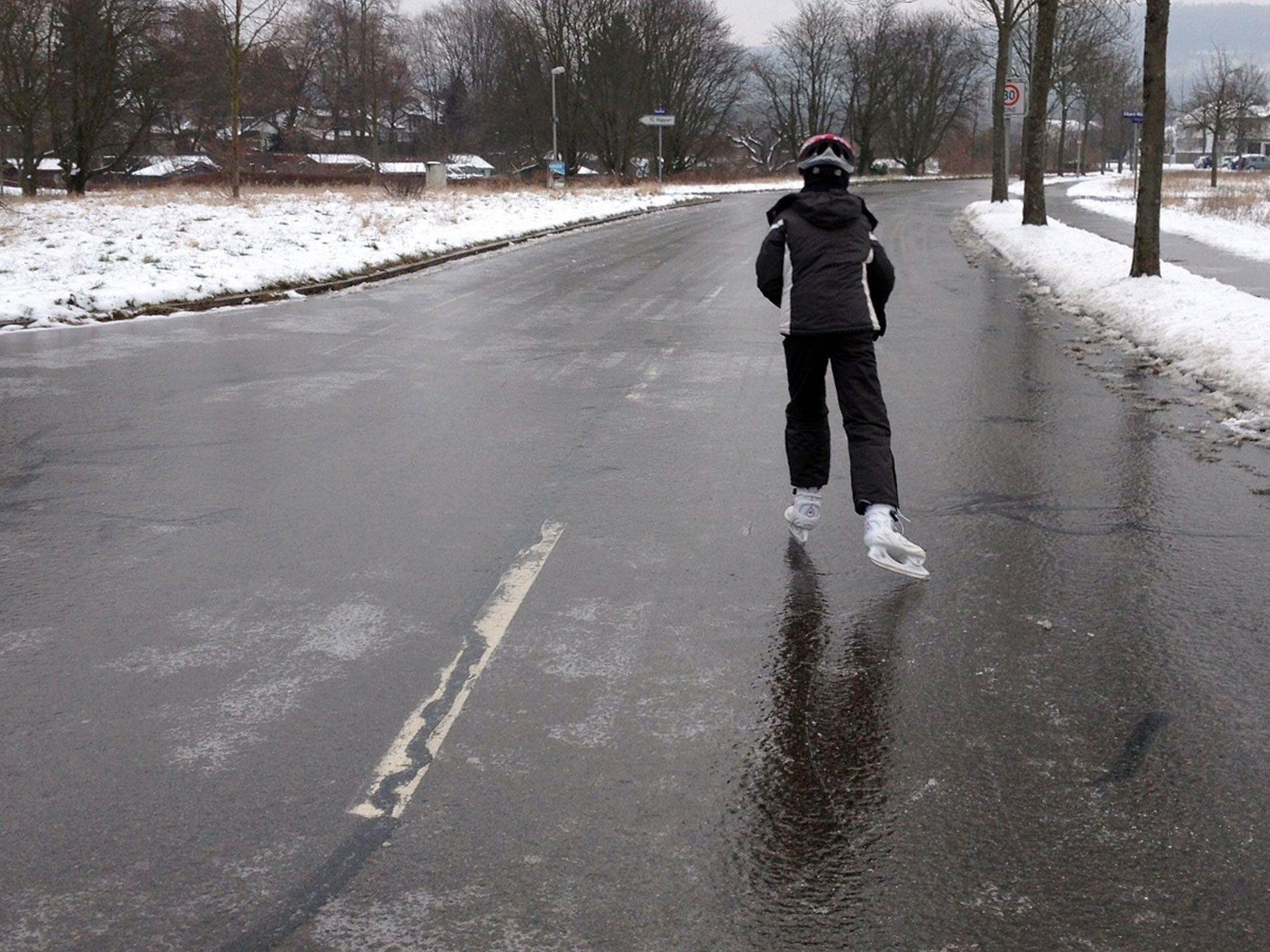 Ein Mann läuft mit Schlittschuhen auf einer durch Blitzeis gefrorenen Straße.