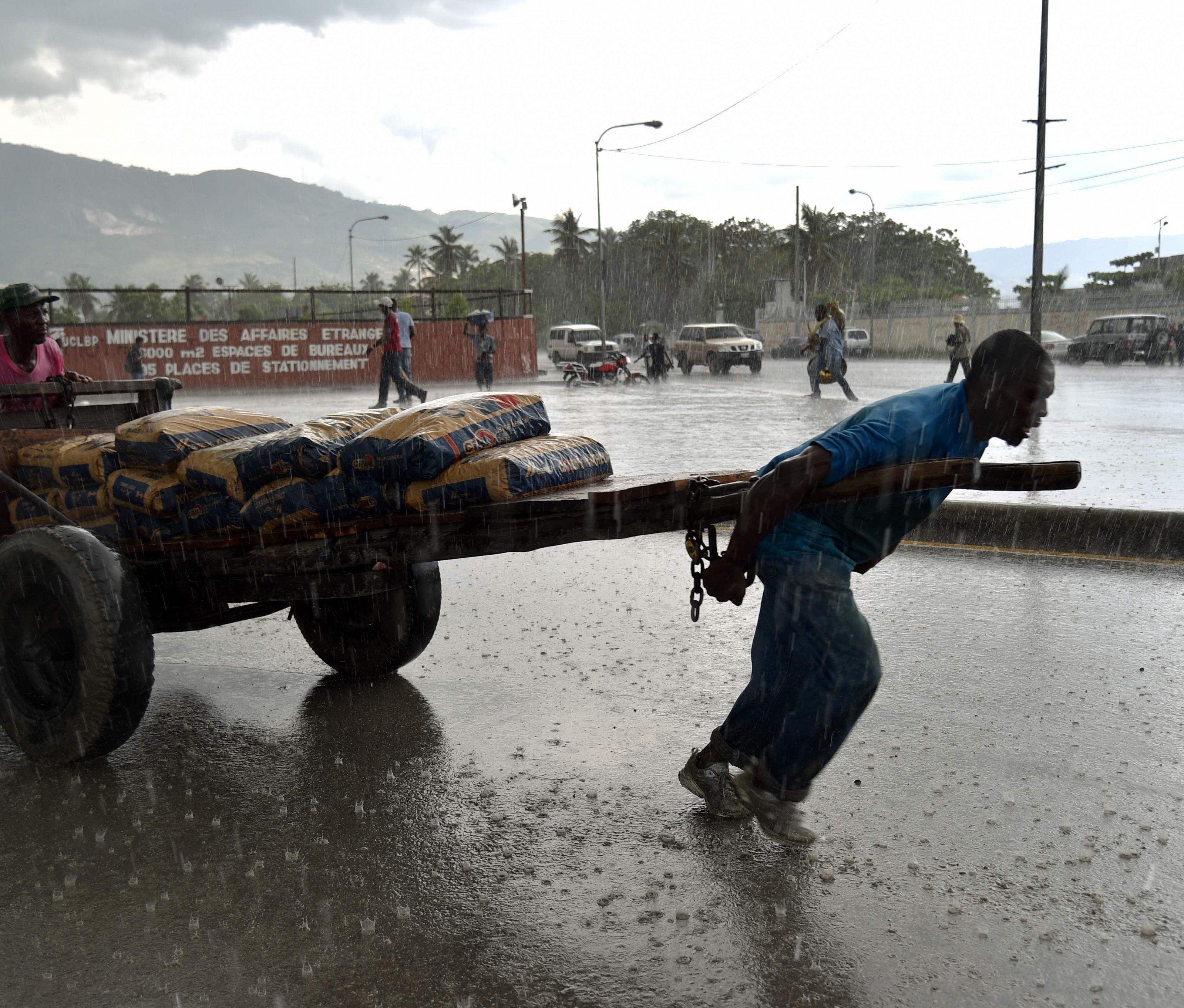 Ein Mann zieht vor dem Parlament in Port-au-Prince einen Karren mit Zement durch den Regen Ein Mann zieht vor dem Parlament in Port-au-Prince einen Karren mit Zement durch den Regen
